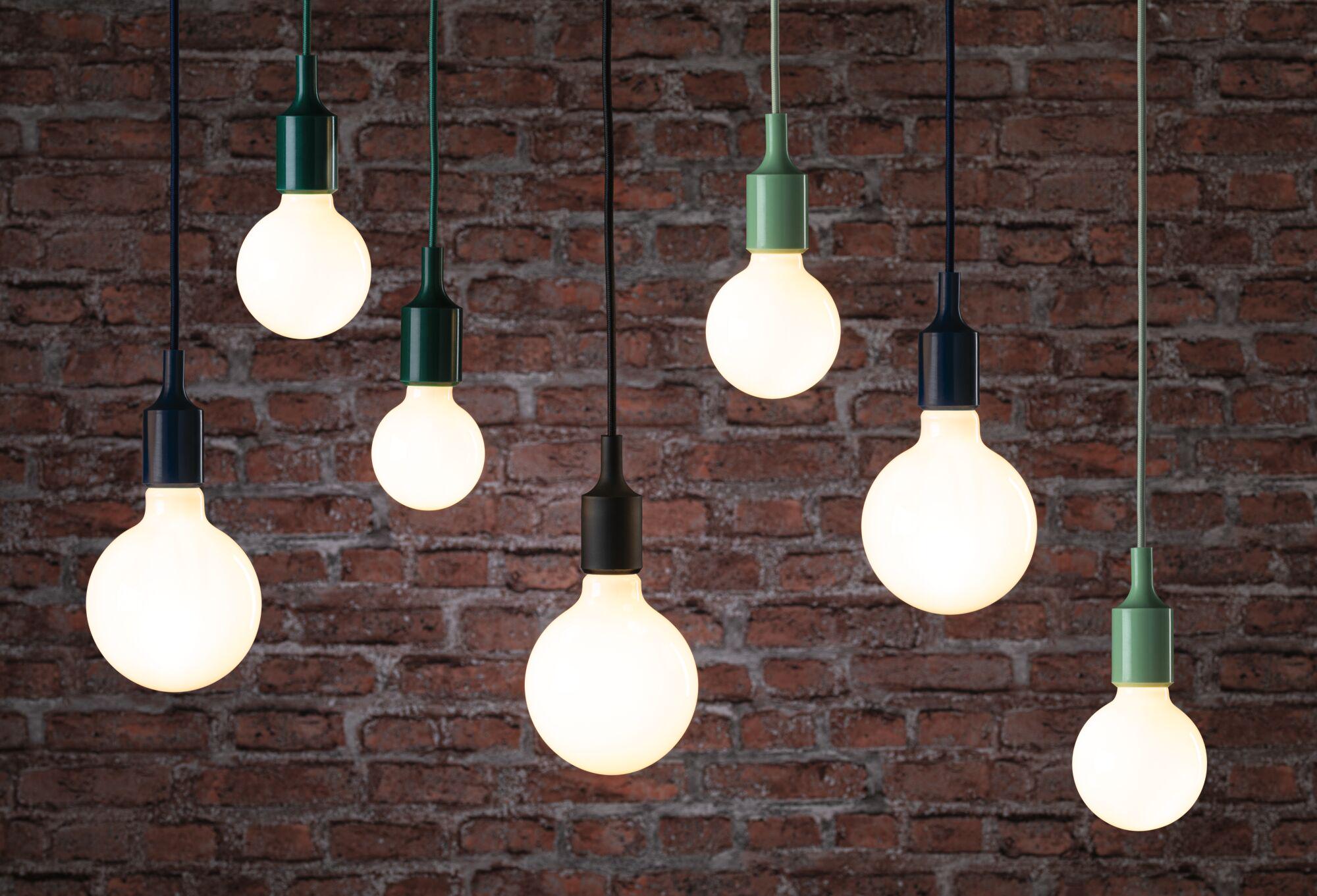 Mehrere hängende LED-Glühbirnen mit schwarzen und grünen Fassungen vor roter Backsteinwand, moderne Beleuchtung