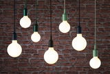 Mehrere hängende LED-Glühbirnen mit schwarzen und grünen Fassungen vor roter Backsteinwand, moderne Beleuchtung