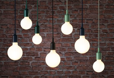 Mehrere hängende LED-Glühbirnen mit schwarzen und grünen Fassungen vor roter Backsteinwand, moderne Beleuchtung