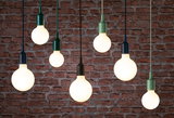 Multiple hanging LED bulbs with colorful sockets against red brick wall, modern pendant lighting.