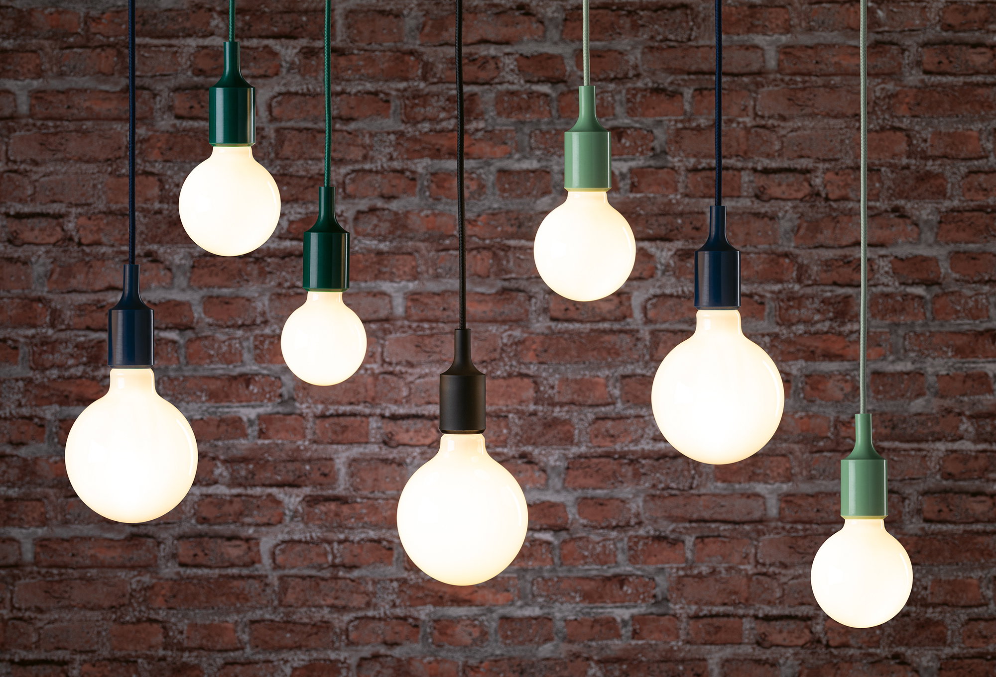 Mehrere hängende LED-Glühbirnen mit bunten Fassungen vor roter Backsteinwand, moderne Pendelleuchten.