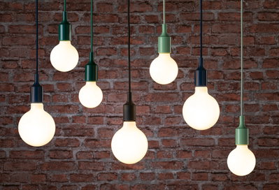 Mehrere hängende LED-Glühbirnen mit schwarzen und grünen Fassungen vor roter Backsteinwand, moderne Beleuchtung