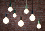 Plusieurs ampoules LED suspendues avec douilles colorées devant un mur en briques rouges, éclairage moderne.