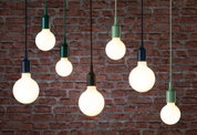 Multiple hanging LED bulbs with colorful sockets against red brick wall, modern pendant lighting.