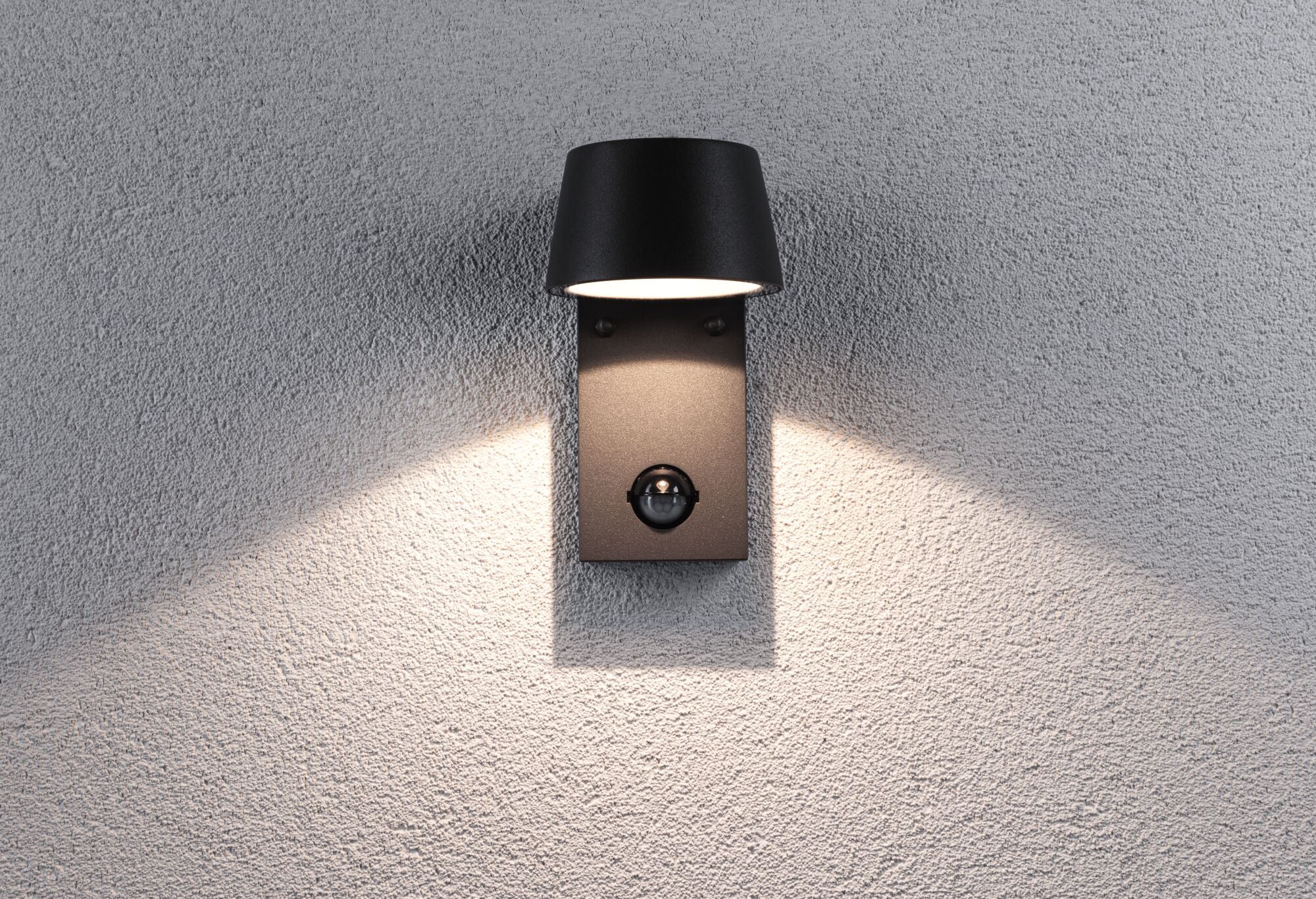 Zwarte metalen buitenwandlamp met bewegingssensor en warm wit licht op grijze muur