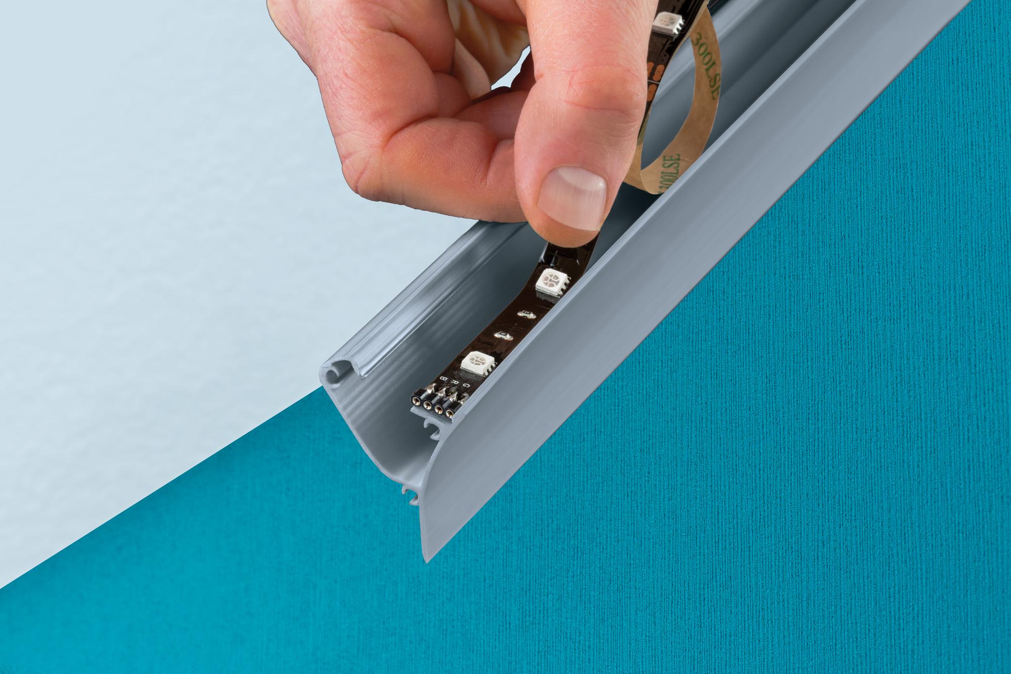 Hånd indsætter sort LED-stribe i gråt aluminiumprofil til vægmontering, LED-belysning