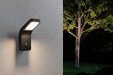 Black LED outdoor wall light with motion sensor mounted on grey wall illuminating garden at night