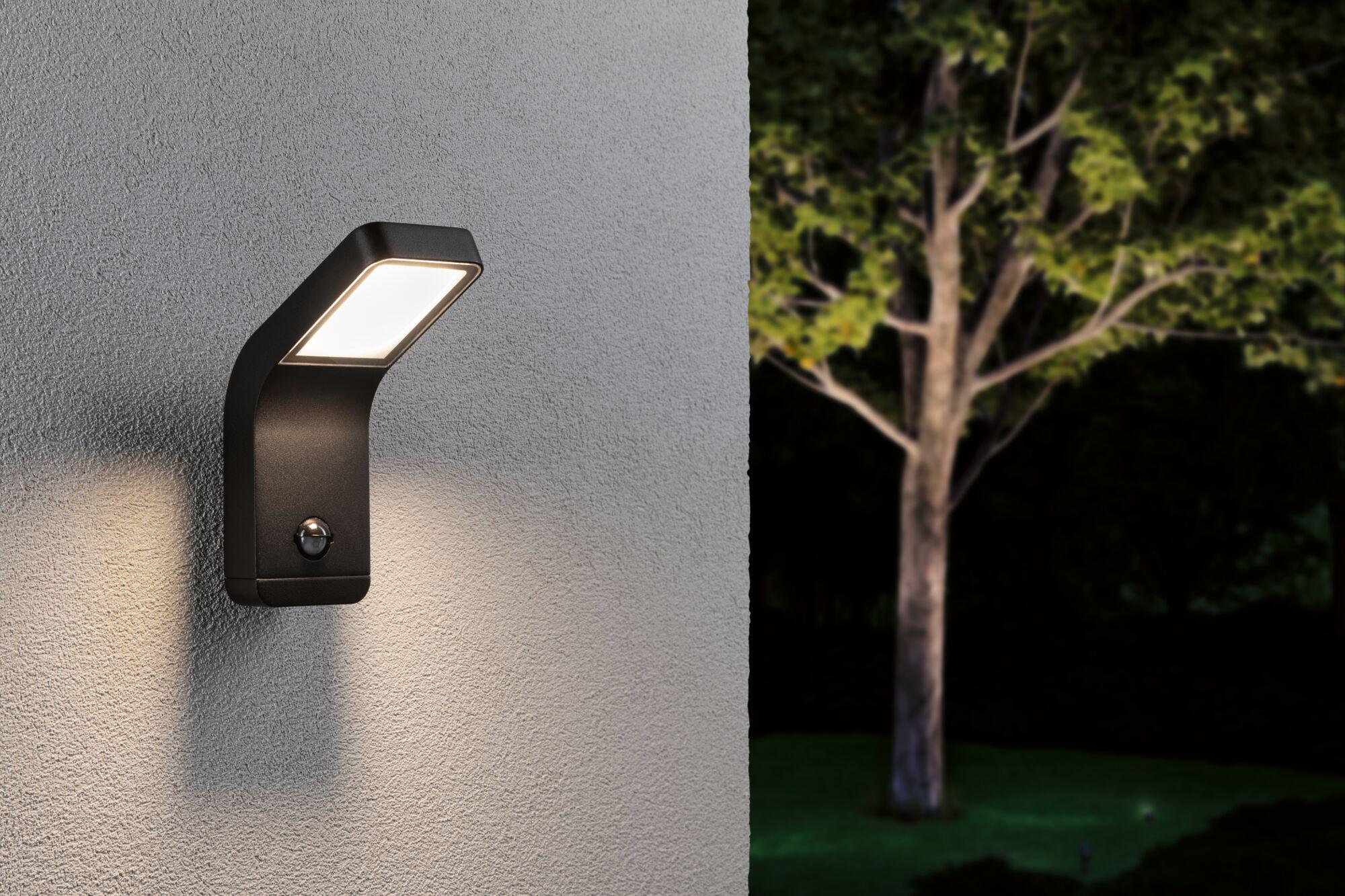 Black metal LED outdoor wall light with motion sensor mounted on grey wall illuminating garden