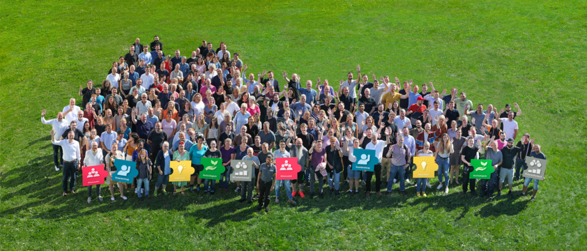 Großes Gruppenfoto von Paulmann Mitarbeitern auf grünem Rasen, symbolisiert Teamarbeit und Unternehmenswerte