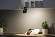 Black LED kitchen clip light on white cabinet illuminating cookbook and fresh herbs on counter.
