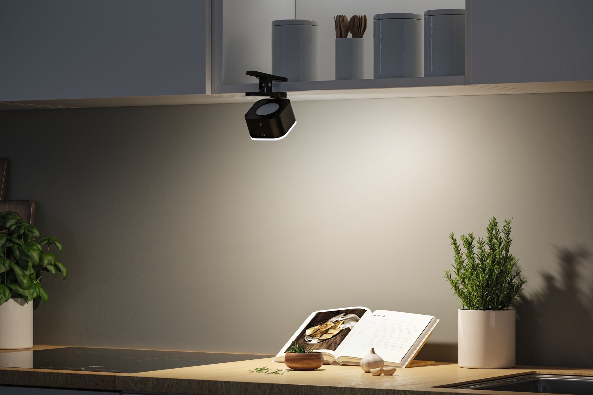 Black LED kitchen clip light on white cabinet illuminating cookbook and fresh herbs on counter.