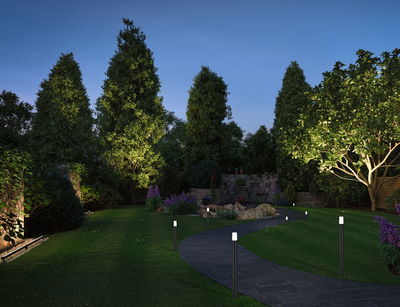 Allée de jardin avec lampes LED noires et arbres verts éclairés en extérieur au crépuscule