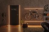 Modern living room with black bike on wall, LED light strips, and brown leather pouf on wooden floor