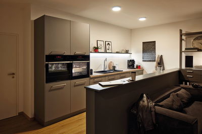 Modern kitchen with built-in black ovens and warm white ceiling lights for ambient home lighting