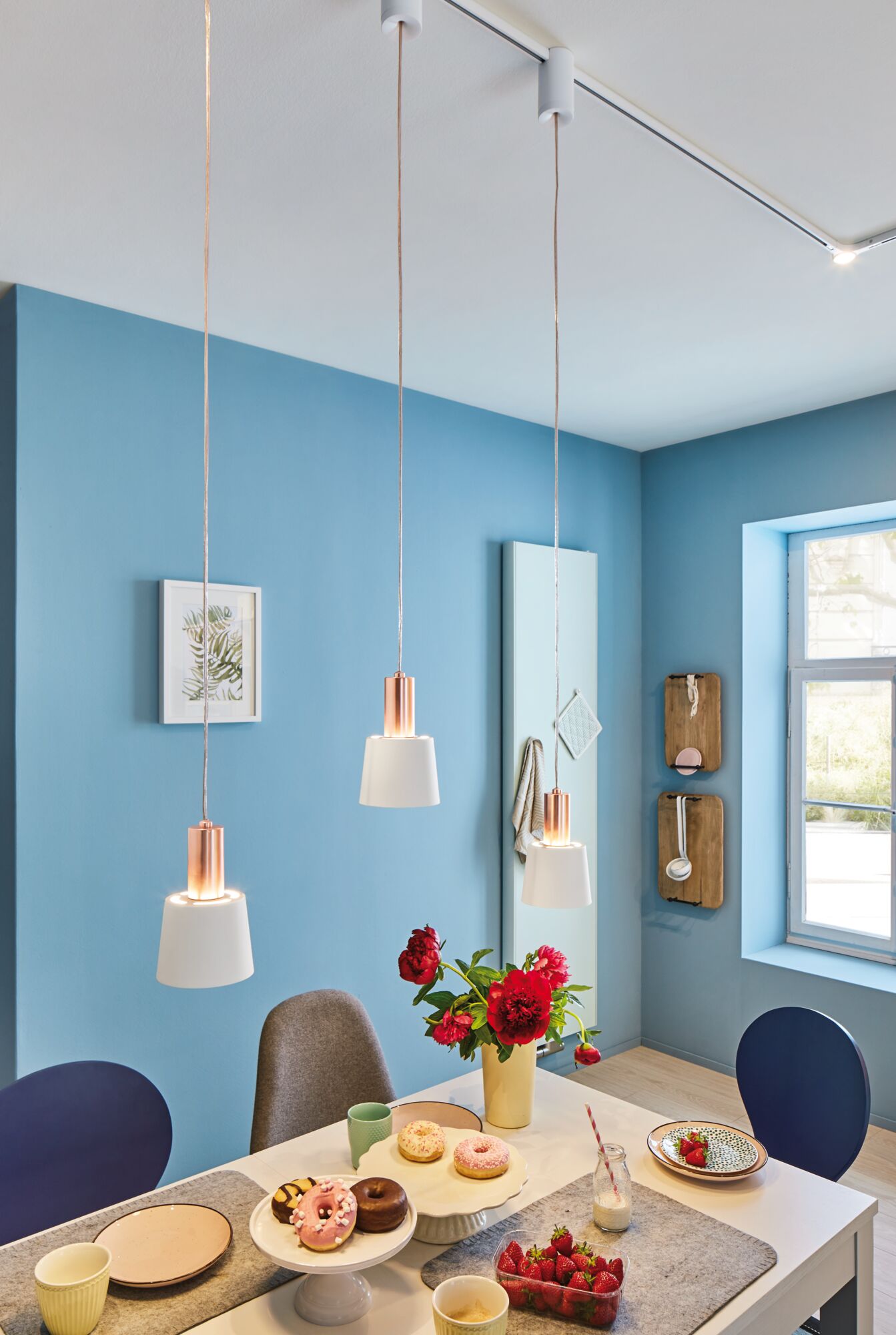 Trois suspensions blanches avec métal cuivre dans salle à manger moderne aux murs bleus et table de petit-déjeuner