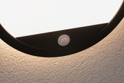 Close-up of round black LED ceiling light with motion sensor mounted on textured wall