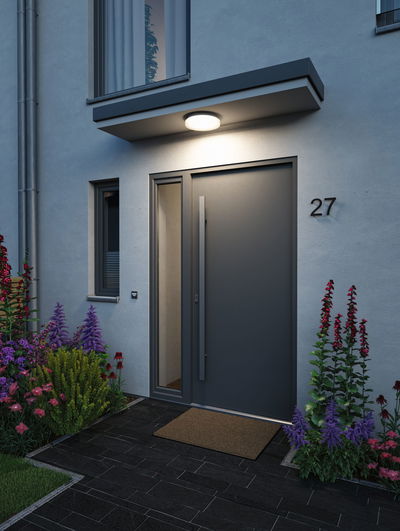 Runde weiße LED-Deckenleuchte aus Kunststoff über Hauseingang mit moderner Tür und Gartenpflanzen