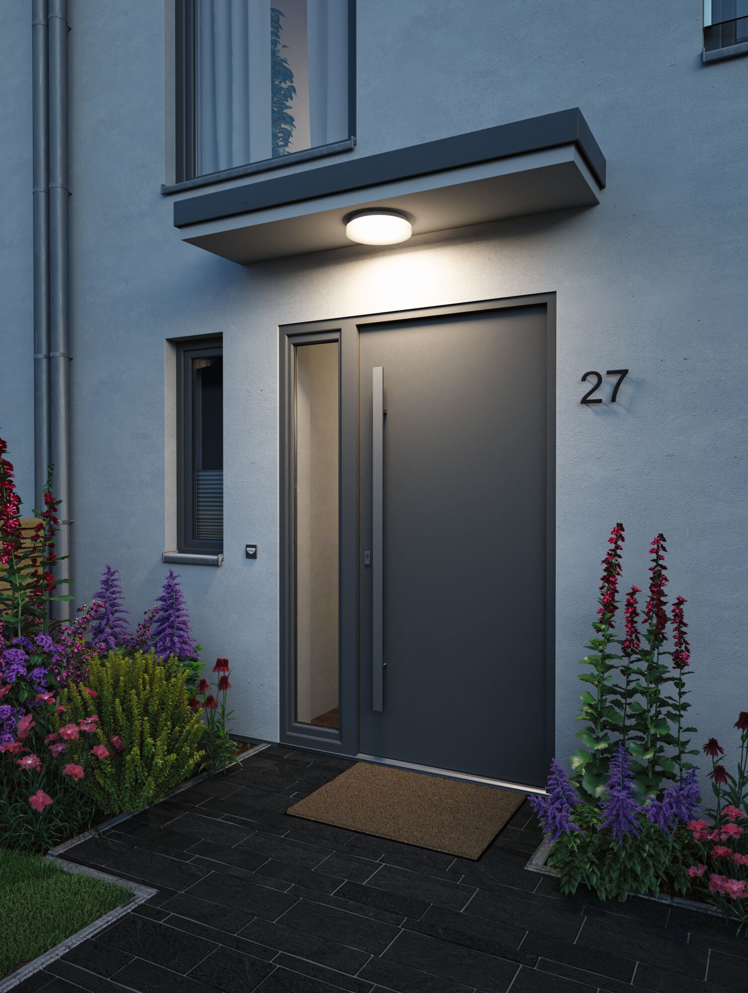 Round white LED ceiling light in plastic above modern house entrance with dark door and garden plants