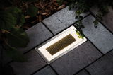 Eingelassene LED-Bodenleuchte mit Edelstahlrahmen und honigwabenförmigem Glas in grauem Pflaster.