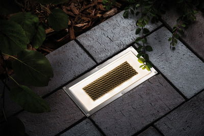 Eingelassene LED-Bodenleuchte mit Edelstahlrahmen und honigwabenförmigem Glas in grauem Pflaster.