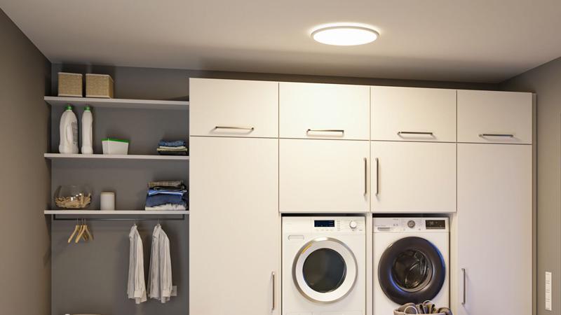 Ronde witte plafondlamp in moderne wasruimte met witte kasten en wasmachine