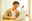 Man in beige cardigan working focused on silver laptop at bright wooden table