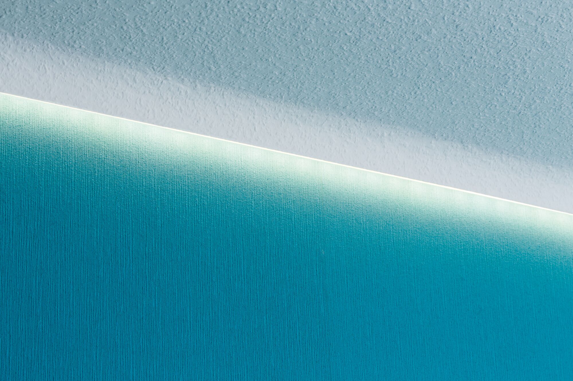 Witte LED-strip aan plafond met indirect licht op blauwe gestructureerde muur voor moderne verlichting