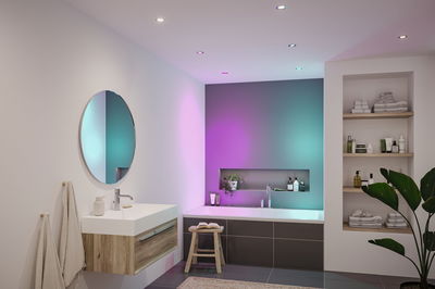Moderne badkamer met ingebouwde LED-plafondlampen in kleurrijk licht en houten wastafel.