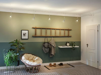 Entrée moderne avec mur vert, porte-manteau en bois échelle et fauteuil rond en rotin avec coussin crème