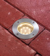 Round stainless steel LED ground recessed light embedded in red pavement for outdoor lighting