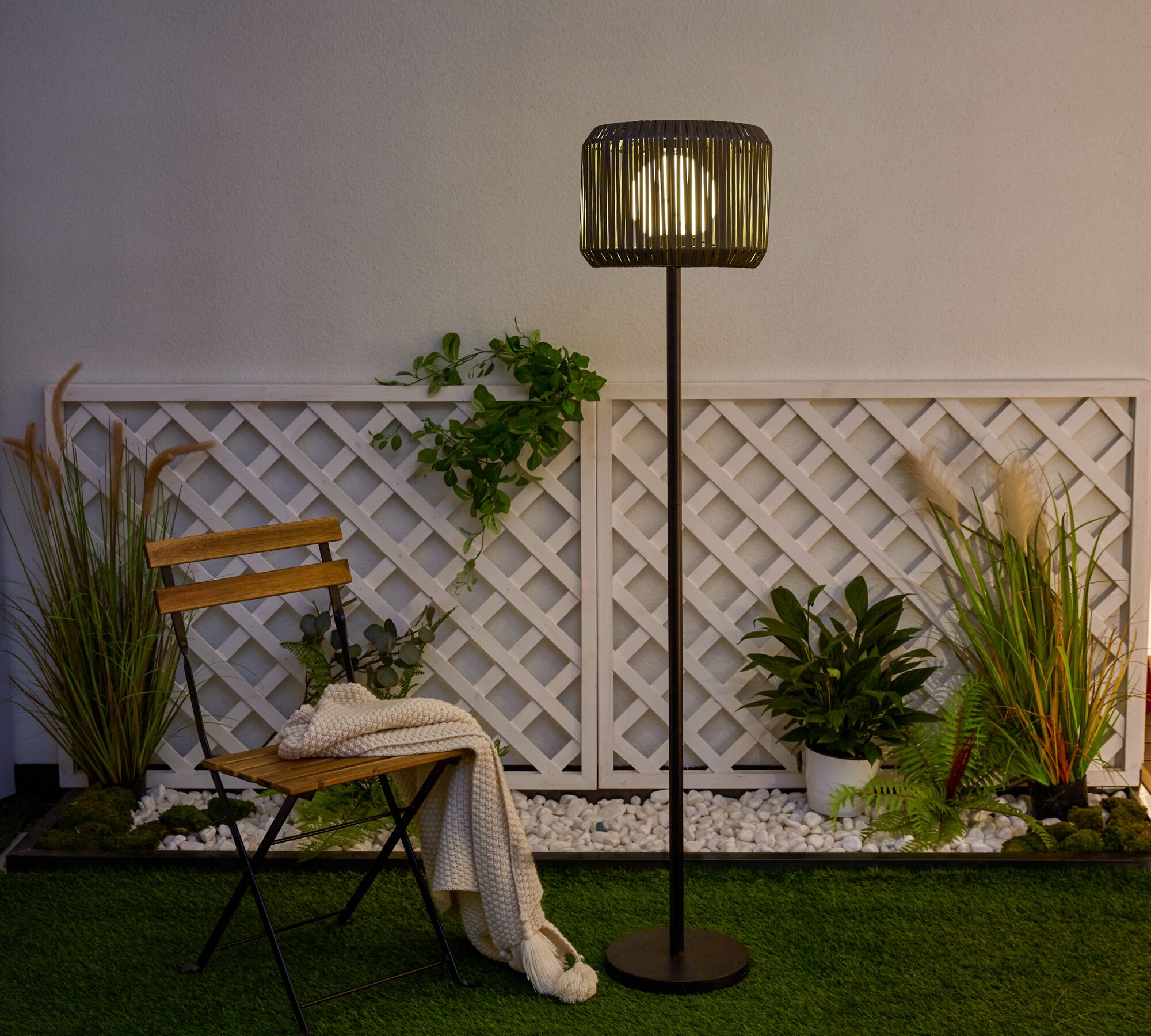 Outdoor standing lamp with black metal frame and wooden slat lampshade in garden setting
