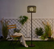 Outdoor standing lamp with black metal frame and wooden slat lampshade in garden setting