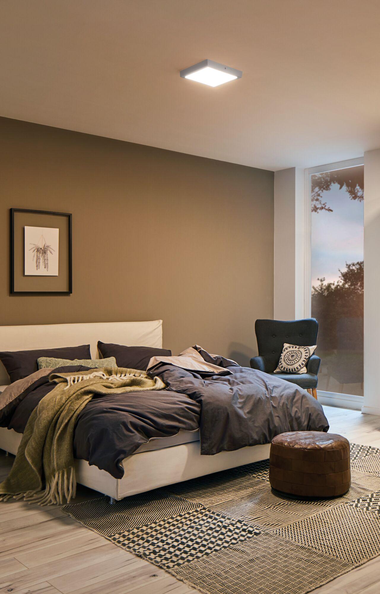 Modern bedroom with white bed, grey bedding, brown leather pouf and ceiling light fixture