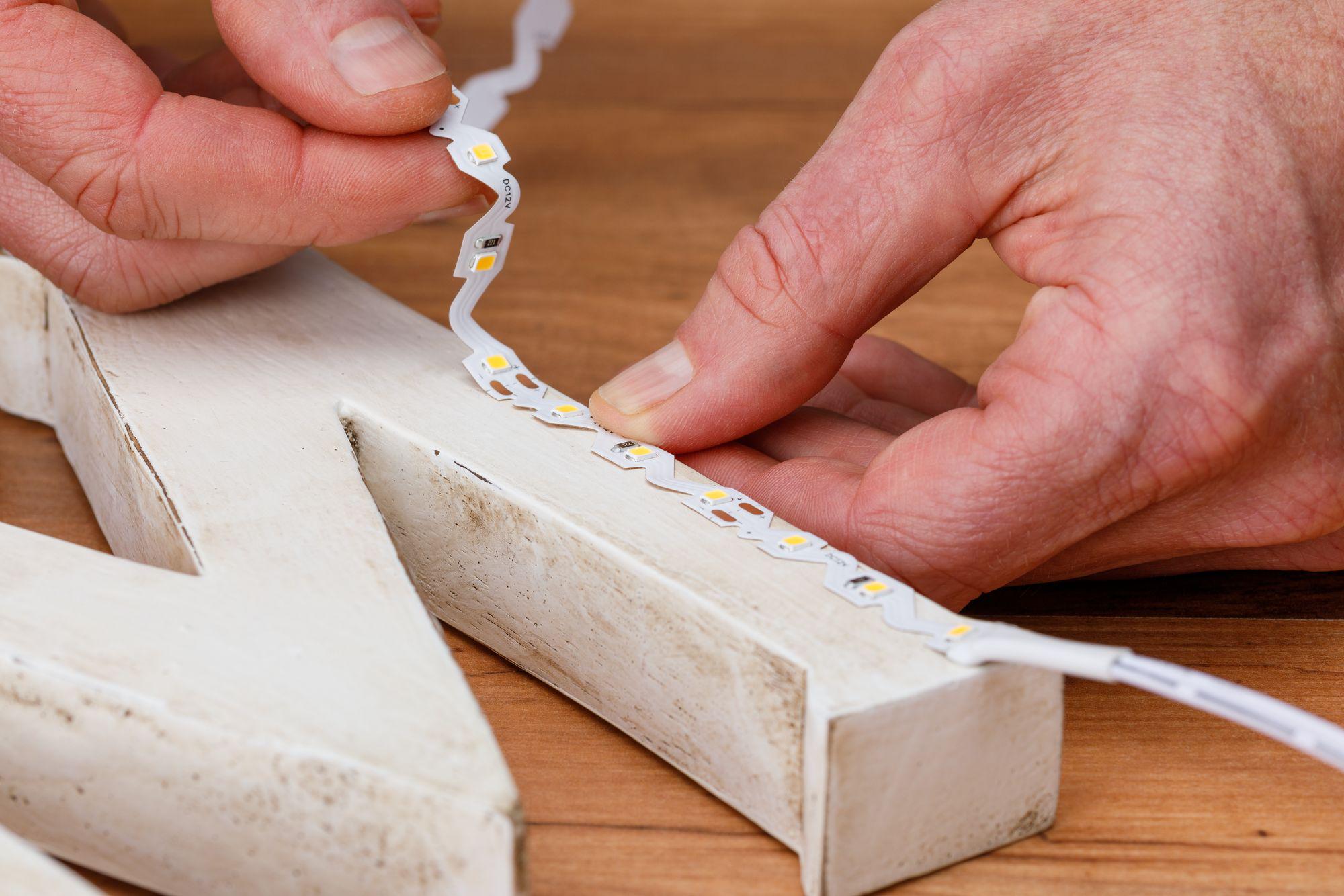 Hand plaatst flexibele witte LED-strip met warmwitte lampjes op witte houten letters
