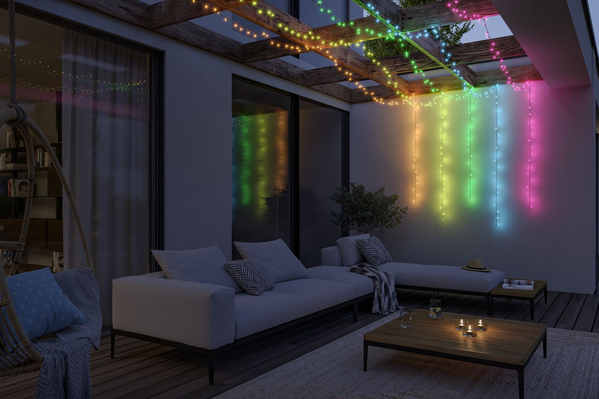 Bunte LED-Lichterketten aus Kunststoff hängen an Holzbalken über moderner Terrasse mit Sofa und Tisch.