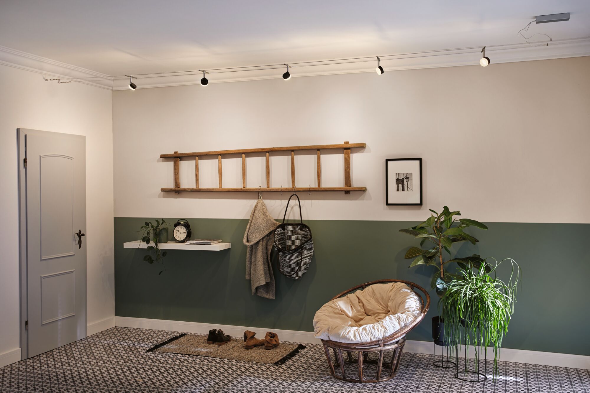 Moderne hal met groene halve muur, houten ladder kapstok en ronde rotan stoel met kussen.