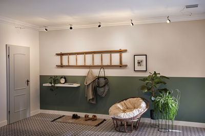 Moderne hal met groene halve muur, houten ladder kapstok en ronde rotan stoel met kussen.