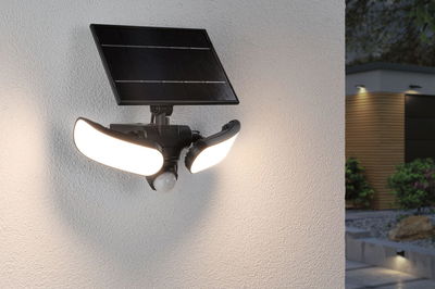 Schwarze Solar-Außenleuchte mit zwei weißen LED-Leuchtflächen und Bewegungsmelder an Hauswand.