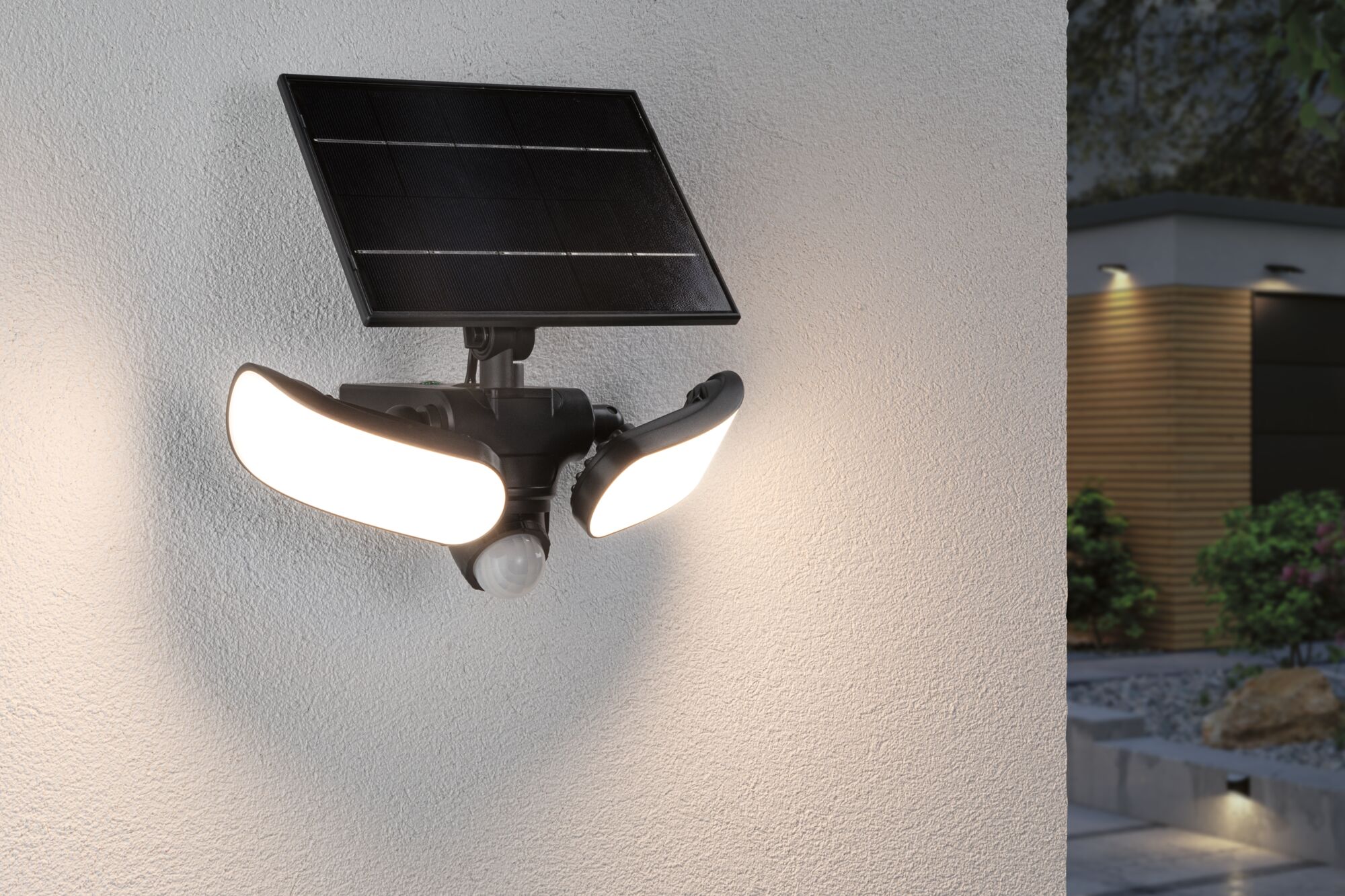 Schwarze Solar-Außenleuchte mit zwei hellen LED-Leuchtflächen und Bewegungsmelder an weißer Wand