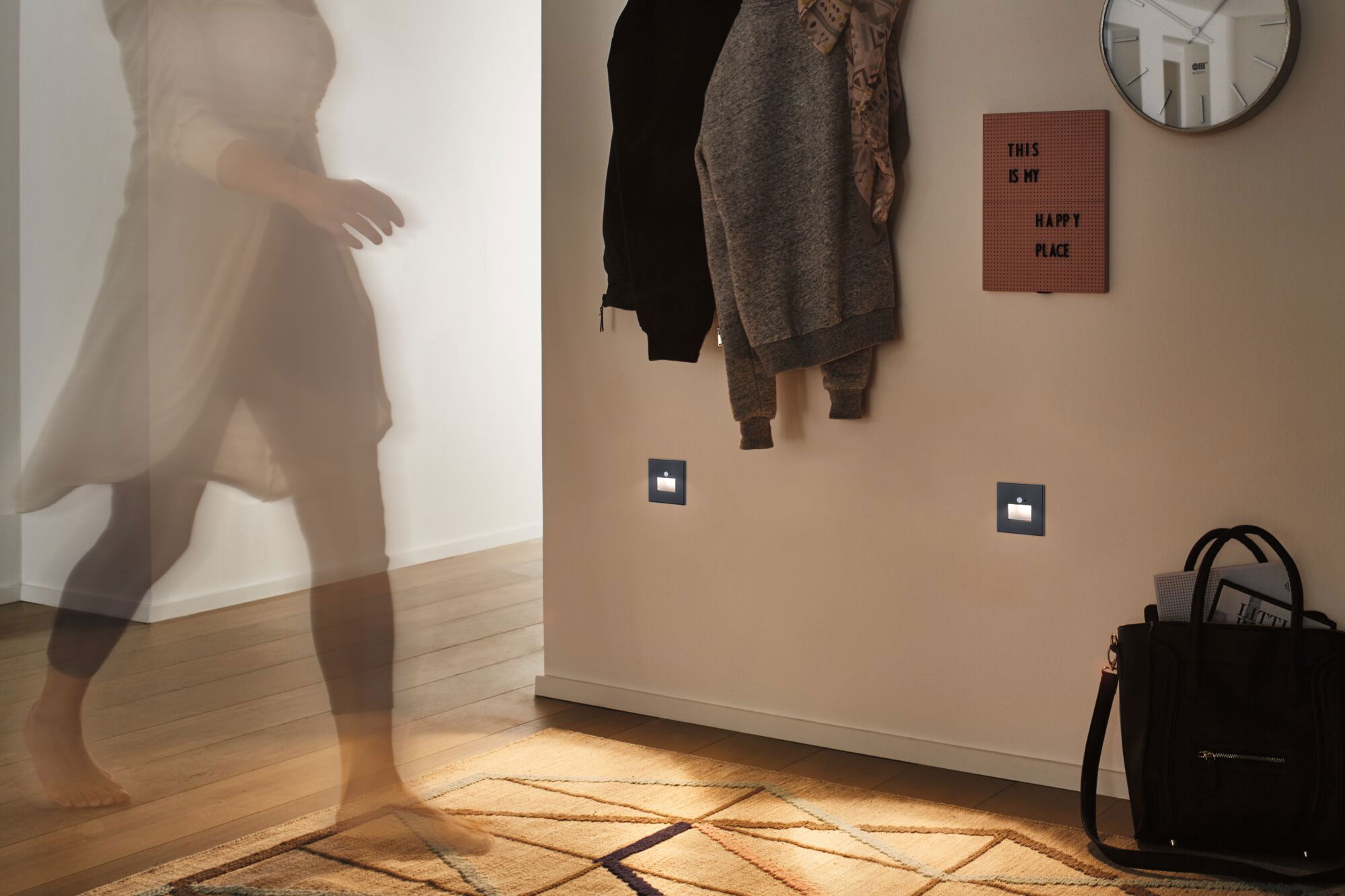 Two square anthracite LED night lights on hallway wall with coat rack and patterned rug.
