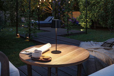 Black metal LED table lamp on wooden garden table with newspaper and coffee cup.
