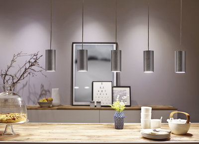 Five brushed aluminum cylindrical pendant lights above wooden table with dishes and vase.