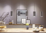 Fünf zylindrische Pendelleuchten aus gebürstetem Aluminium über Holztisch mit Geschirr und Vase.