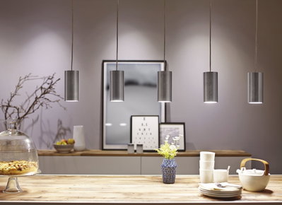Fünf zylindrische Pendelleuchten aus gebürstetem Aluminium über Holztisch mit Geschirr und Vase.