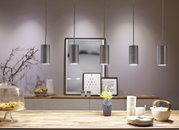 Five brushed aluminum cylindrical pendant lights above wooden table with dishes and vase.