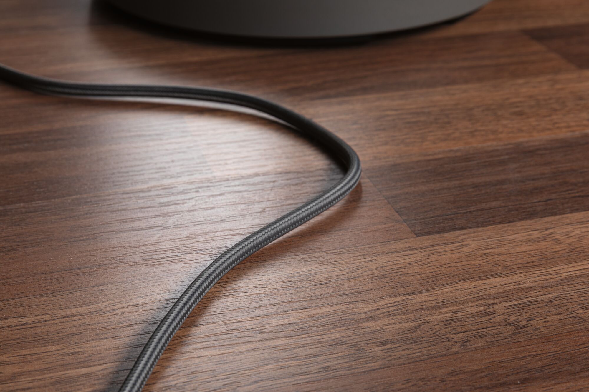 Close-up of black fabric-covered cable on brown wooden floor, suitable for lighting cable use