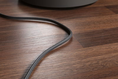 Close-up of black fabric-covered cable on brown wooden floor, suitable for lighting cable use