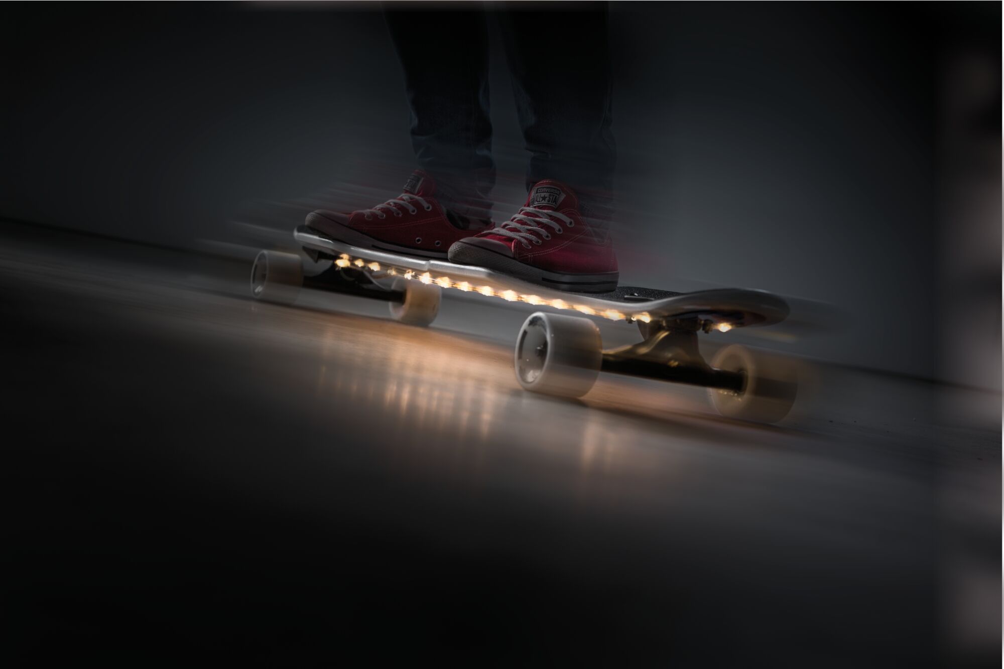 Skateboard avec roues blanches et éclairage LED sous la planche, personne en chaussures rouges à l'intérieur.
