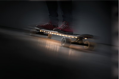 Skateboard avec roues blanches et éclairage LED sous la planche, personne en chaussures rouges à l'intérieur.