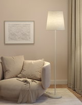 Beige vloerlamp met stoffen kap naast ronde bank en abstracte wanddecoratie in woonkamer